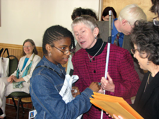 Pictured here, Rogina Melvin receives her Braille Readers Are Leaders packet and certificate from Jill Lewis. Sharon Maneki congratulates her while Barbara Cheadle looks on smiling. This party was for student contest participants from the Maryland School for the Blind.