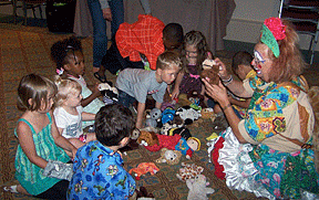 Children sit engrossed as a clown tells them a story using puppets.