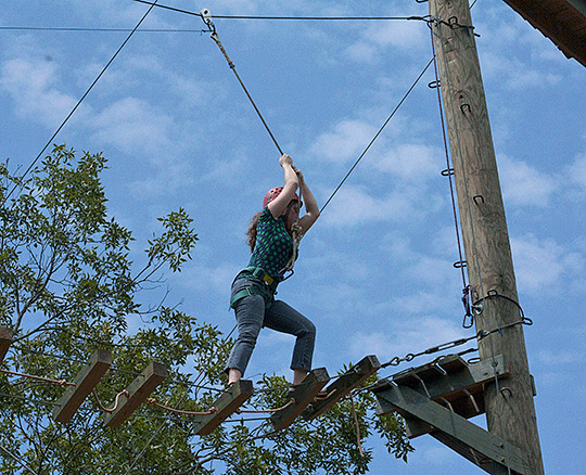 Amber Attaway, above it all, walks along a bouncy skybridge made of planks and wires.