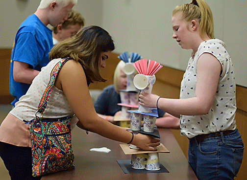 Two girls investigate the tower of cups and construction paper they will have to duplicate for copycat towers.