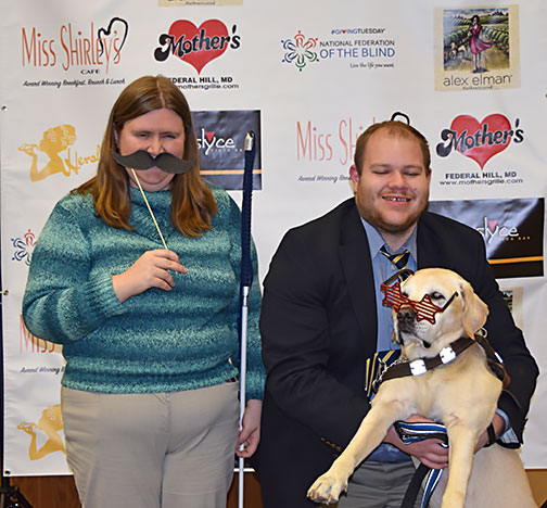 Amy Mason rocks a handheld mustache while Karl Belanger holds his guide dog, Quasar up to model a pair of star-shaped sunglasses in the photo booth