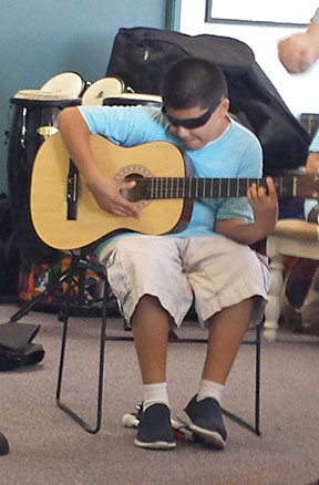 David sits in a chair playing an acoustic guitar.
