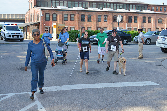 Rose Sloan walks in a group with a man using a guide dog, several others using canes, and a woman pushing a stroller.