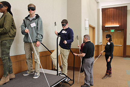 Chris Danielsen coaxes students and a teacher with Art of Leadership up-stairs while using canes and wearing sleepshades.
