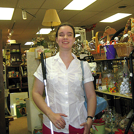 The girl holds her cane, standing among shelves loaded with collectibles.