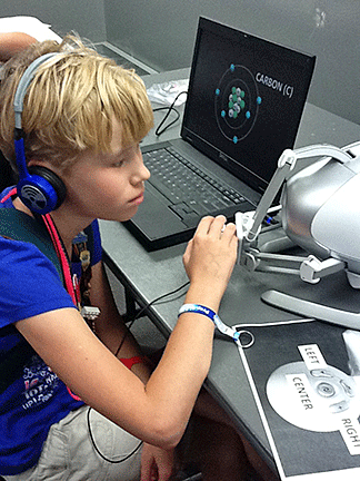 A girl wearing headphones uses the haptic device to examine carbon atoms.