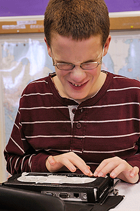 The young student reads Braille with his notetaker.