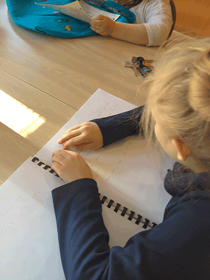 A little girl reads a Braille book.