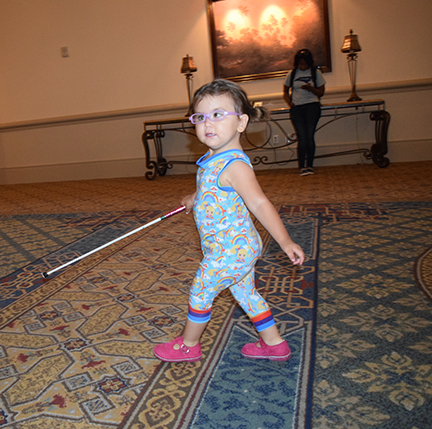 A girl with a cane walks down a hotel corridor.