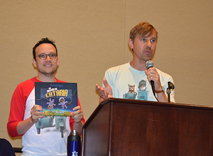 Travis Brossard and Mick Szydlowski stand at a podium, holding up their book, The Mission to Cataria.
