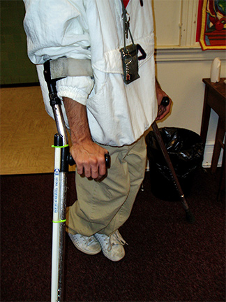 A man uses crutches along with a long white cane.